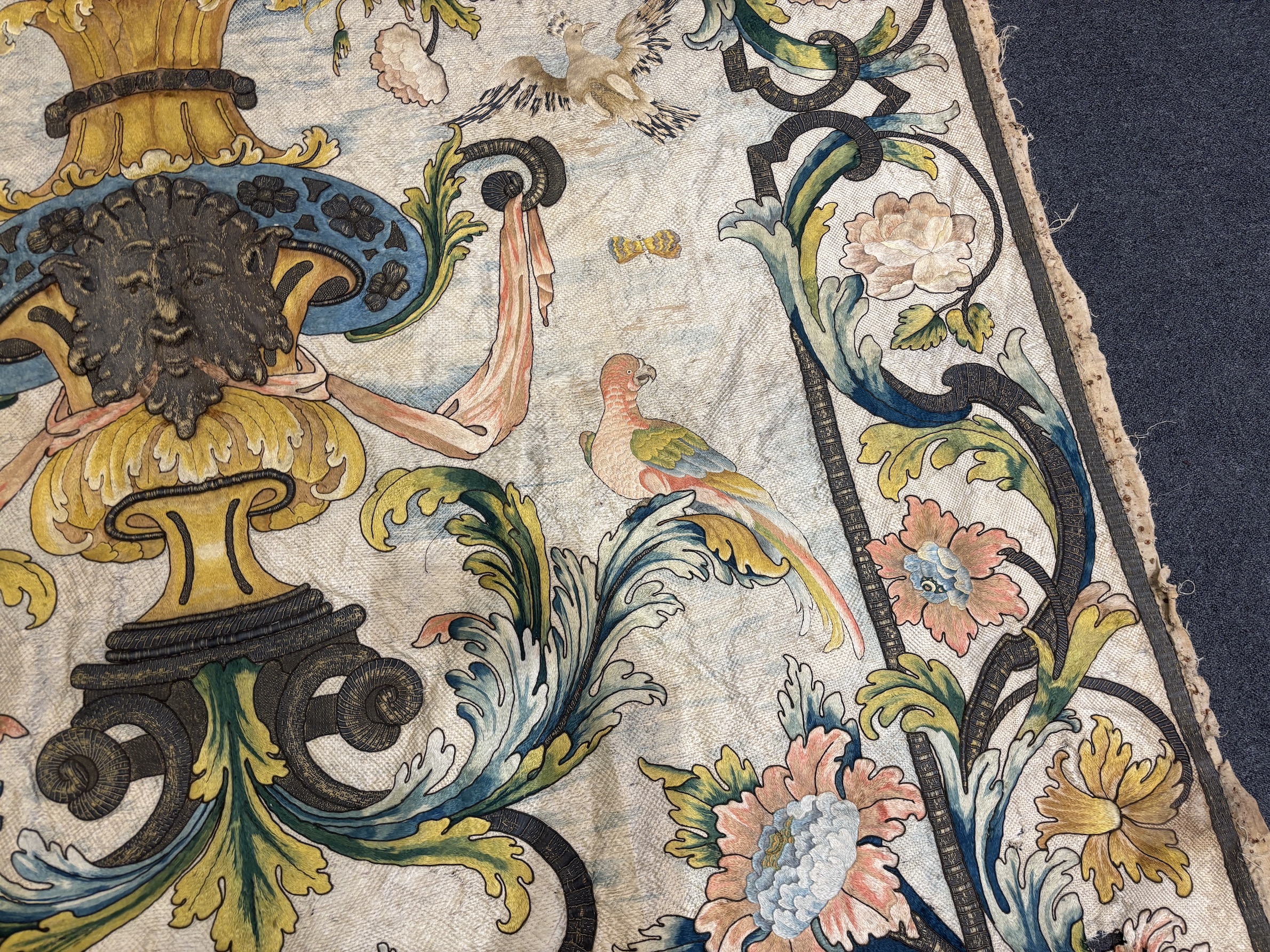 A large early 18th century possibly French polychrome and gold metallic silk embroidered wall hanging, with scrolling vine and floral border. The central motifs embroidered with an elaborate metallic thread cartouche fra